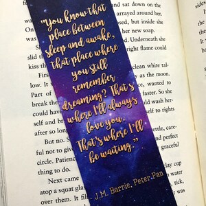 K&ouml;nnte beinhalten: Ein violettes und blaues Lesezeichen mit goldenen Glitzersternen und Text. Der Text lautet: "Du kennst diesen Ort zwischen Schlaf und Wachsein, diesen Ort, an dem du dich noch an das Tr&auml;umen erinnerst? Dort werde ich dich immer lieben. Dort werde ich warten." Das Lesezeichen enth&auml;lt auch den Text "J.M. Barrie, Peter Pan."