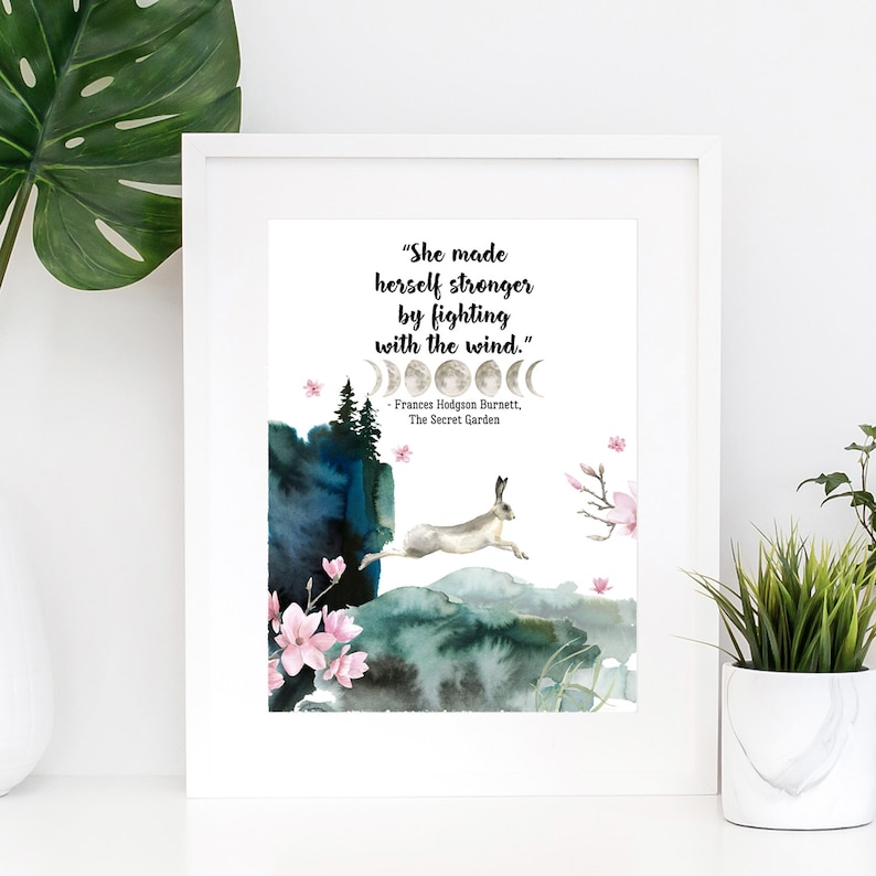 Puede incluir: Una impresi&oacute;n de acuarela con una cita de Frances Hodgson Burnett, de El jard&iacute;n secreto. La cita dice: "Se hizo m&aacute;s fuerte luchando contra el viento." La impresi&oacute;n presenta una ilustraci&oacute;n de acuarela de un conejo blanco saltando sobre una colina con un bosque en el fondo. La ilustraci&oacute;n est&aacute; rodeada por un borde blanco.