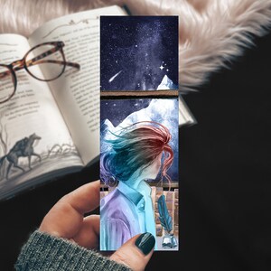 May include: A watercolour bookmark depicting a woman with long, flowing hair gazing out of a window at a starry night sky. The woman is wearing a blue and purple shirt and the window is framed by a wooden sill.