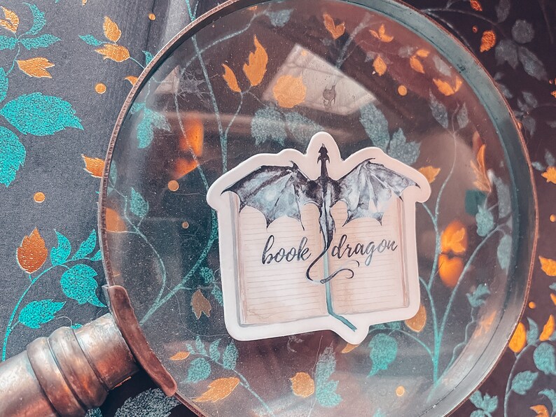 May include: A sticker featuring a black and white illustration of a dragon emerging from a book with the text "book dragon".