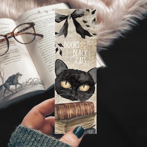 May include: A decorative bookmark featuring a black cat with yellow eyes, the text "BOOKS & BLACK CATS", and a stack of books. The bookmark is held in front of an open book with glasses.
