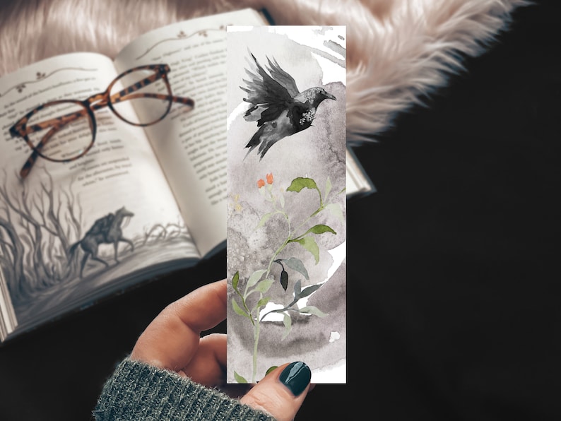 May include: A watercolour bookmark featuring a black crow flying over a branch with green leaves and orange berries. The background is a grey wash.