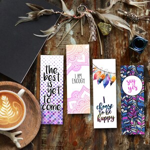 Peut inclure: Ensemble de quatre marque-pages colorés avec des citations inspirantes. Les marque-pages présentent une variété de motifs, notamment des motifs géométriques, des plumes et des mandalas. Les citations sur les marque-pages sont "Le meilleur est à venir", "Je suis assez", "Je choisis d'être heureux", et "Dis oui".