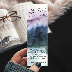 Puede incluir: Un marcapáginas de acuarela con una cita de George R.R. Martin sobre la lectura. La cita dice: "Un lector vive mil vidas antes de morir. El hombre que nunca lee solo vive una."