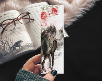 May include: A black unicorn with a white horn and mane stands on a white background with pink and red watercolor flowers. The unicorn is painted in a watercolor style with a soft, dreamy look.