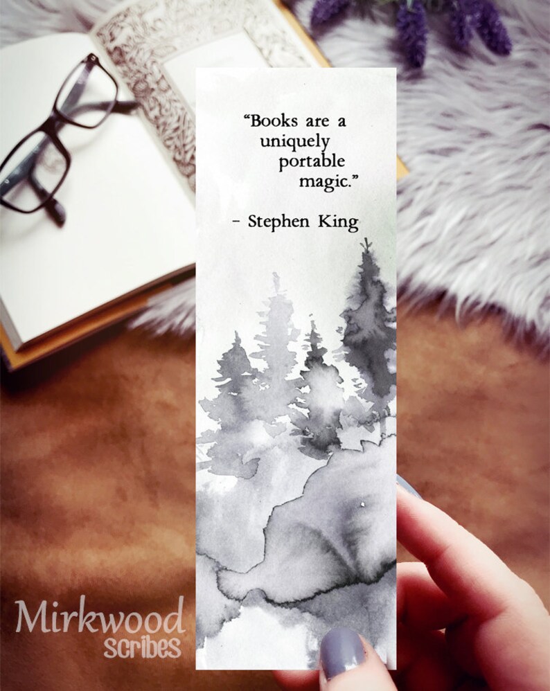 Puede incluir: Un marcap&aacute;ginas de acuarela en blanco y negro con una cita de Stephen King: "Los libros son una magia port&aacute;til &uacute;nica." La cita est&aacute; impresa sobre un fondo blanco con una ilustraci&oacute;n de acuarela de un bosque.