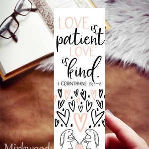 May include: White bookmark with black text that reads "LOVE is patient LOVE is kind. 1 Corinthians 13:4-8". The bookmark is decorated with pink hearts and two white bunnies holding a jar with a pink heart inside.