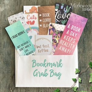 May include: A white envelope with the text "Bookmark Grab Bag" printed on the front. The envelope is filled with colorful bookmarks with various designs and text, including "I read books. Not because I don't have a life. Because I...", "Cats", "Book", "Coffee", "Blan", "But first, Coffee", "Love", and "A book a day keeps reality away!"