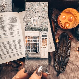 Peut inclure: Peinture &agrave; l'aquarelle d'un petit b&acirc;timent en briques avec une enseigne qui indique "Cafe" et "Book". Le b&acirc;timent a une grande fen&ecirc;tre avec un chat noir assis dans la fen&ecirc;tre. Le b&acirc;timent est peint dans des tons de brun, gris et vert.