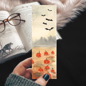 May include: A watercolor bookmark featuring a field of orange pumpkins with bats flying overhead. The background is a hazy, blue sky with a silhouette of a forest in the distance.
