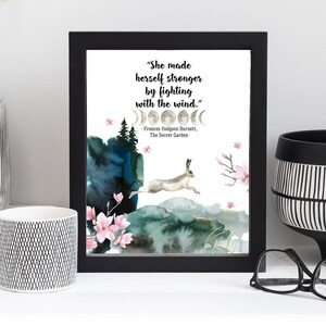 Puede incluir: Una impresi&oacute;n enmarcada en negro con un fondo blanco que presenta una cita de Frances Hodgson Burnett's The Secret Garden. La cita dice "She made herself stronger by fighting with the wind." La impresi&oacute;n tambi&eacute;n presenta una ilustraci&oacute;n de acuarela de una liebre saltando sobre una colina con un dise&ntilde;o de fase lunar arriba.