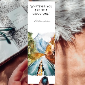 May include: A watercolor bookmark featuring a road leading to a mountain, with autumn foliage. The bookmark has the quote "WHATEVER YOU ARE, BE A GOOD ONE." by Abraham Lincoln. A book and glasses are in the background.
