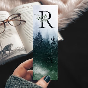 May include: A watercolor bookmark with a forest scene and the letter "R" in a black font. The background is a blue and green gradient with white stars.