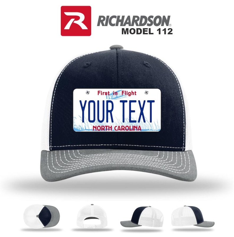 May include: A navy blue and white trucker hat with a gray brim. The hat features a rectangular patch with the text "YOUR TEXT" and "NORTH CAROLINA" on it. The patch also has the text "First in Flight".