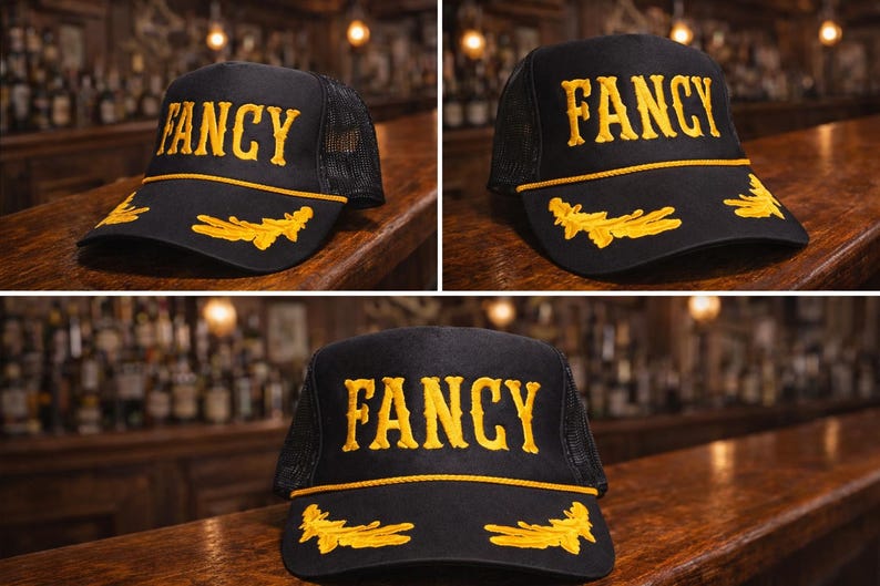 May include: A black trucker hat featuring the word FANCY embroidered in yellow on the front panel. The brim is decorated with yellow embroidered leaf motifs and a yellow cord trim. The back portion of the hat is constructed from black mesh fabric.