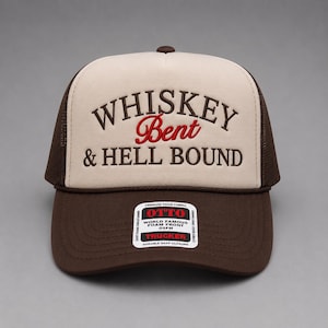 May include: A brown and tan trucker hat with the words "Whiskey Bent & Hell Bound" embroidered on the front in brown and red. The hat has a mesh back and a curved brim. The hat is made of foam fabric.