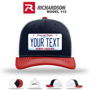 May include: A Richardson Model 112 trucker hat with a navy blue crown, white mesh back, and red brim. The hat features a custom license plate design with the text "YOUR TEXT" and "NORTH CAROLINA".