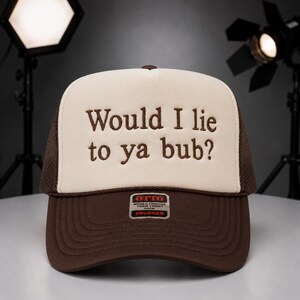 May include: A brown and beige trucker hat with the embroidered text "Would I lie to ya bub?" The hat has a mesh back and a curved brim. The hat has a tag that says "OTTO World Famous Foam Front Trucker".