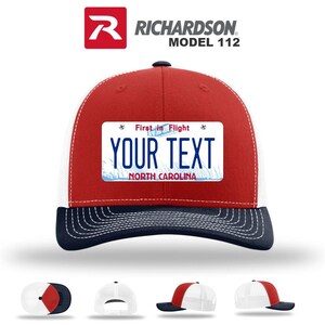 May include: A red, white, and navy blue Richardson Model 112 trucker hat. The hat features a white mesh back, a red front panel, and a navy blue brim. A rectangular patch on the front displays the text "YOUR TEXT" above "NORTH CAROLINA".