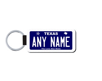 May include: A white keychain with a blue Texas license plate design. The plate says "TEXAS" and "ANY NAME" with a star and the state outline. The text "The Lone Star State" is below the name.