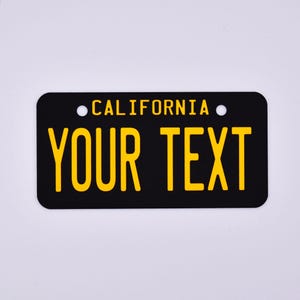 May include: Black and yellow California license plate with the text "YOUR TEXT" printed in yellow.