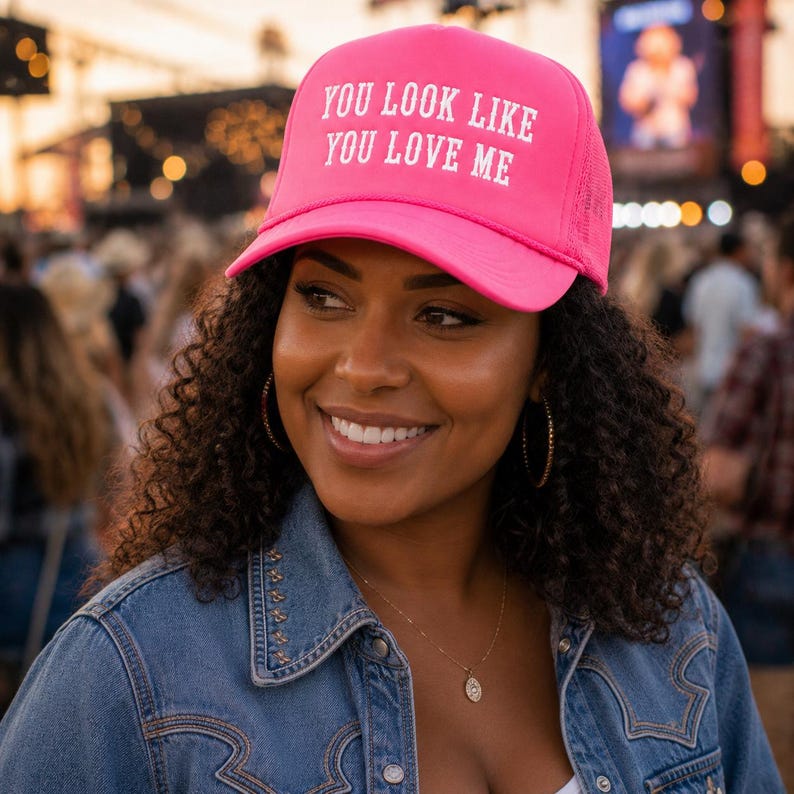 May include: A bright pink trucker hat featuring the white embroidered text "YOU LOOK LIKE YOU LOVE ME" on the front panel. The cap has a structured foam front, a curved brim, and a mesh back panel, designed with a classic adjustable snapback closure.