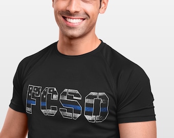 May include: A black t-shirt with a white graphic of the word "F.I.S.D." in a distressed font. The letters are made up of an American flag design with a blue line running through the middle of each letter.