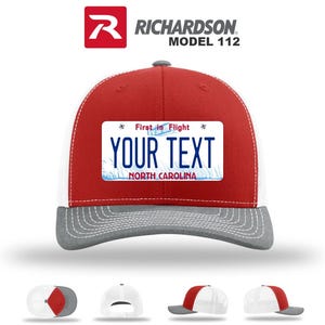 May include: A red, white, and gray Richardson Model 112 trucker hat. The front panel features a license plate design with the text "YOUR TEXT" and "NORTH CAROLINA". The hat has a curved brim and a mesh back.