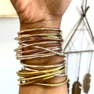 May include: A stack of gold and rose gold bangle bracelets on a person's wrist. The bracelets are arranged in a criss-cross pattern.