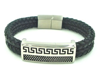 May include: A black braided leather bracelet featuring a rectangular silver-tone metal centerpiece. The centerpiece displays a black Greek key pattern on the top half and a dotted texture on the bottom half, secured by a silver-tone magnetic clasp.