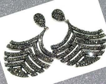 May include: A pair of elegant, dark gray dangle earrings. Each earring features a teardrop-shaped top and a fan-like design composed of multiple curved rows. The earrings are adorned with small, sparkling embellishments, creating a glamorous look.