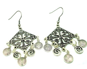 May include: A pair of silver-toned dangle earrings featuring a square filigree charm with a central cross-like pattern. Each earring is adorned with multiple small, circular charms hanging from the bottom edge, each etched with a spiral design.