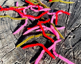 May include: A close-up of a pile of pink and red fishing lures with a brown wooden background.