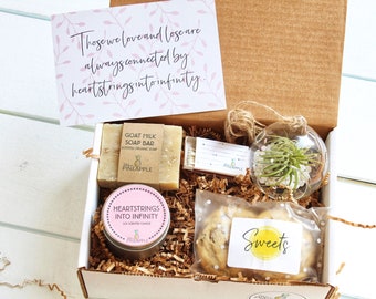 May include: A gift box filled with a variety of items, including a candle, soap, a small plant in a glass orb, cookies, and a card with the quote "Those we love and lose are always connected by heartstrings into infinity."