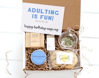 May include: A gift box filled with birthday presents, including a candle, soap, cookies, and a small plant in a glass globe. The box has a card on top that says "Adulting is fun! Said no one ever. Happy birthday anyway."