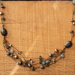 May include: A multi-strand necklace with brown, green, and blue beads. The necklace is made of multiple strands of beads and wire, and is hanging on a wooden surface.