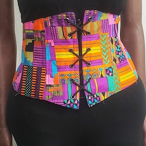 May include: A colorful, patterned corset with a lace-up front. The corset is made of a bright fabric with geometric shapes in shades of pink, purple, orange, yellow, green, and black. The laces are black.