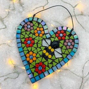 May include: A heart-shaped mosaic tile ornament with a bee design. The bee is made of black, yellow, and white tiles. The heart is surrounded by green, blue, red, and pink tiles.