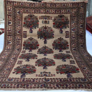 May include: A large, rectangular beige rug with a repeating pattern of stylized trees in vases. The trees are depicted in shades of red, blue, and brown. The rug has a detailed border with geometric designs and fringe along the edges.