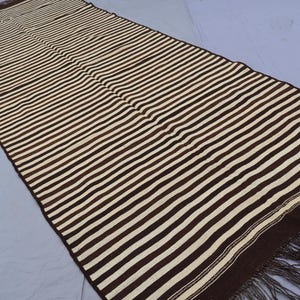 May include: A brown and white striped rug with fringe on the ends. The rug is made of a woven material and has a traditional design.