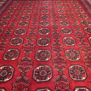 May include: A large, rectangular red rug with an intricate geometric pattern. The rug features repeating octagonal shapes with detailed floral designs in shades of brown, cream, and black. The border is a darker shade of red.