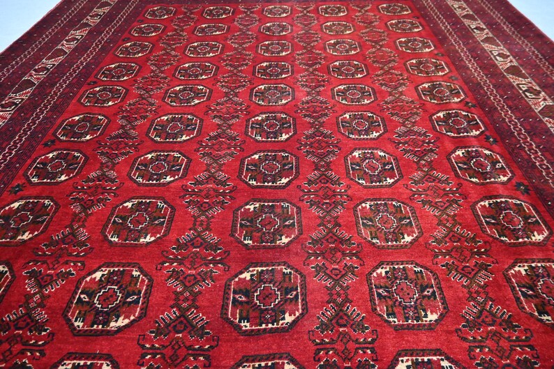 May include: A large, rectangular red rug with an intricate geometric pattern. The rug features repeating octagonal shapes with detailed floral designs in shades of brown, cream, and black. The border is a darker shade of red.