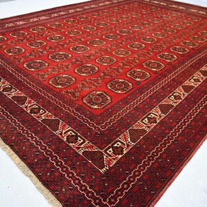 May include: A rectangular, red oriental rug with a detailed geometric pattern. The rug features a central field of repeating circular motifs in shades of brown and tan, framed by a border with intricate designs. The rug's dimensions are approximately 8 x 10 feet.