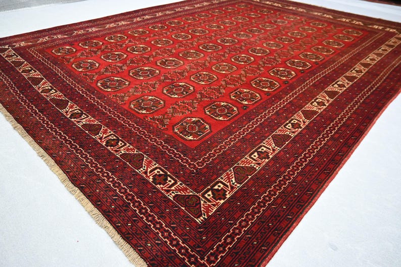 May include: A rectangular, red oriental rug with a detailed geometric pattern. The rug features a central field of repeating circular motifs in shades of brown and tan, framed by a border with intricate designs. The rug's dimensions are approximately 8 x 10 feet.