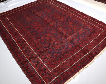 May include: A rectangular area rug featuring a deep red and dark blue geometric pattern. The design consists of repeating motifs within a central field, surrounded by a wide border with intricate linear details and short white fringe at the ends.