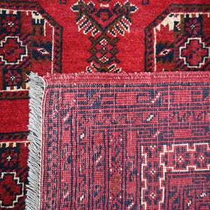 May include: Close-up of a red oriental rug with intricate geometric patterns in navy blue, white, and brown. The rug has a detailed border and a fringed edge, showcasing traditional craftsmanship.