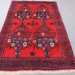 Può includere: Un tappeto rettangolare rosso con un design floreale dettagliato. Il tappeto presenta un motivo centrale di alberi stilizzati con accenti floreali blu e bianchi. Il bordo è blu scuro con motivi floreali e una frangia color crema.