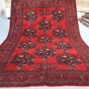 Può includere: Un tappeto rosso con un design persiano tradizionale che presenta un motivo ripetuto di alberi stilizzati con motivi floreali. Il tappeto ha un bordo blu scuro con intricati motivi geometrici.