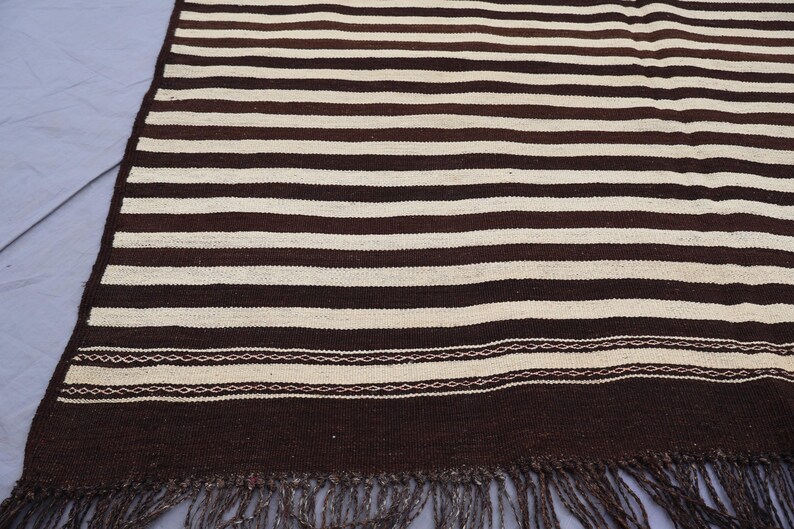 May include: A brown and white striped woven rug with fringe. The rug has a simple design with alternating stripes of brown and white.