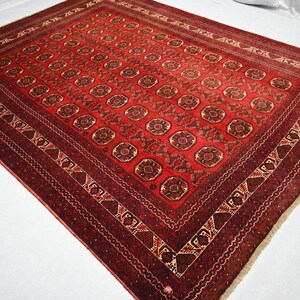 May include: A rectangular, red oriental rug with a repeating geometric pattern. The rug features a central field of repeating medallions and a detailed border in shades of red, brown, and cream. The rug's dimensions are not visible.